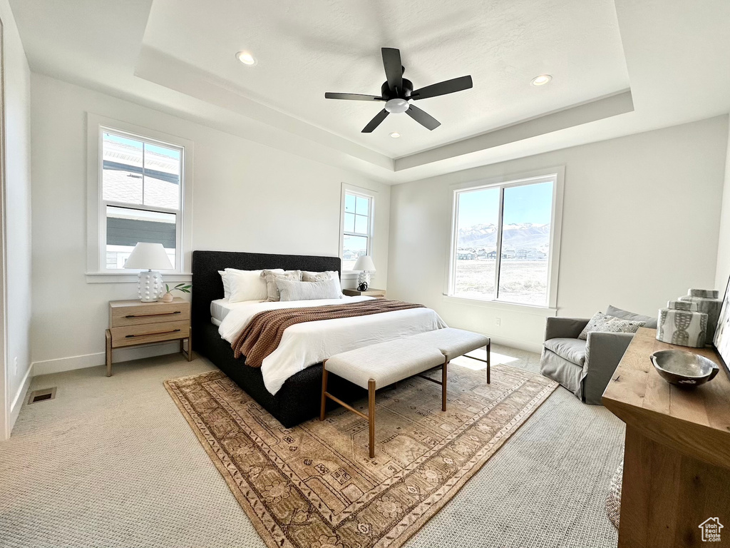 Bedroom with ceiling fan, light carpet, and a raised ceiling