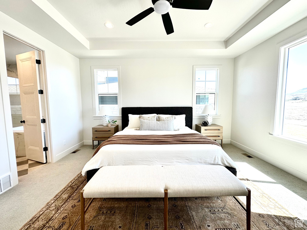 Bedroom with ceiling fan, light carpet, a tray ceiling, and multiple windows