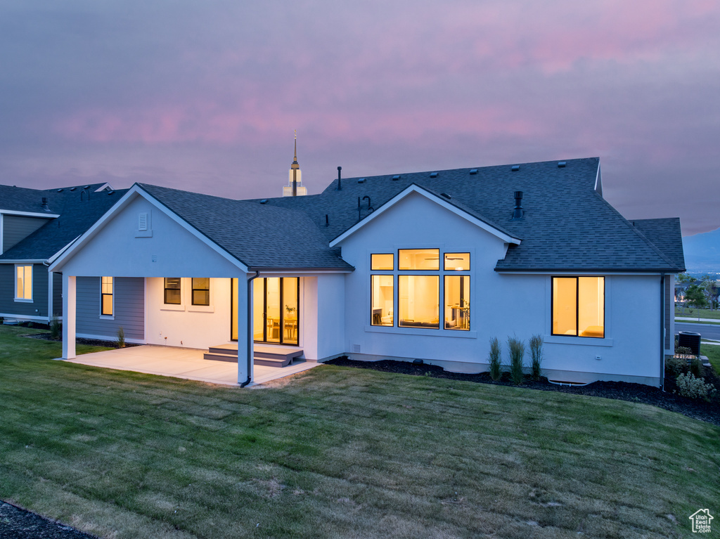 Back house at dusk with a patio and a lawn