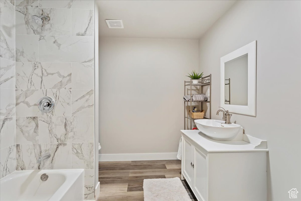 Full bathroom featuring hardwood / wood-style flooring, large vanity, tiled shower / bath combo, and toilet