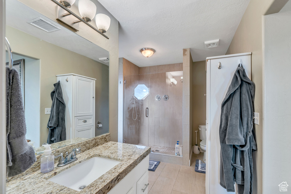 Bathroom featuring a textured ceiling, vanity, toilet, a shower with shower door, and tile flooring