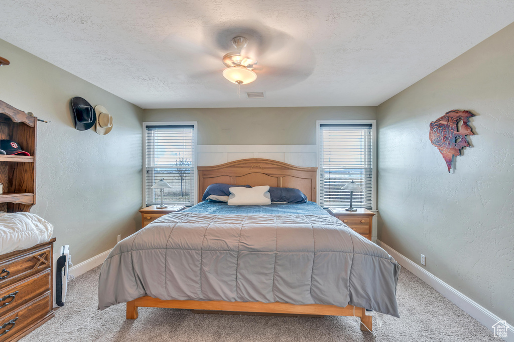 Carpeted bedroom featuring ceiling fan, a textured ceiling, and multiple windows