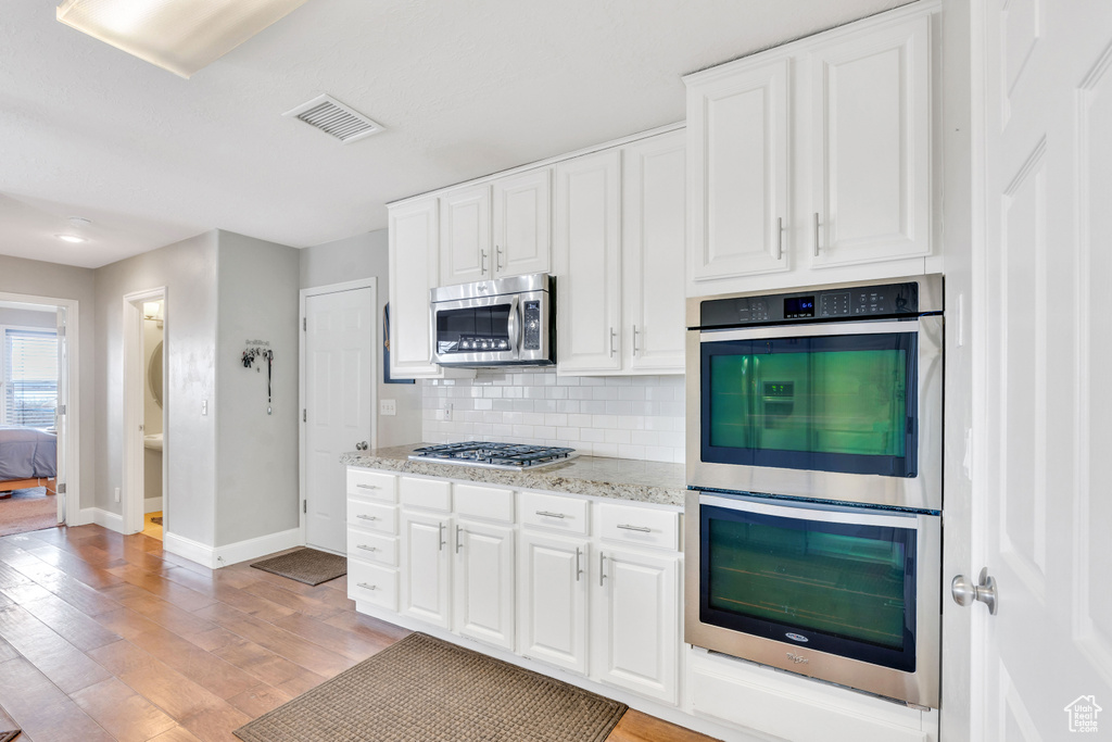 Kitchen featuring appliances with stainless steel finishes, light hardwood / wood-style flooring, light stone counters, and white cabinets