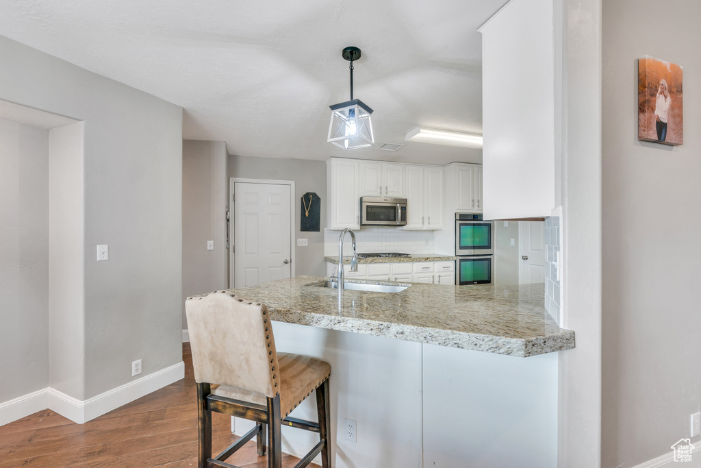Kitchen with hardwood / wood-style floors, pendant lighting, stainless steel appliances, white cabinetry, and sink