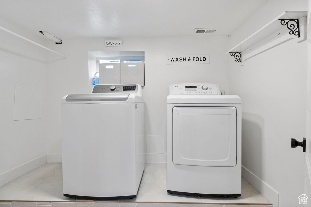 Washroom with light tile flooring and washing machine and clothes dryer