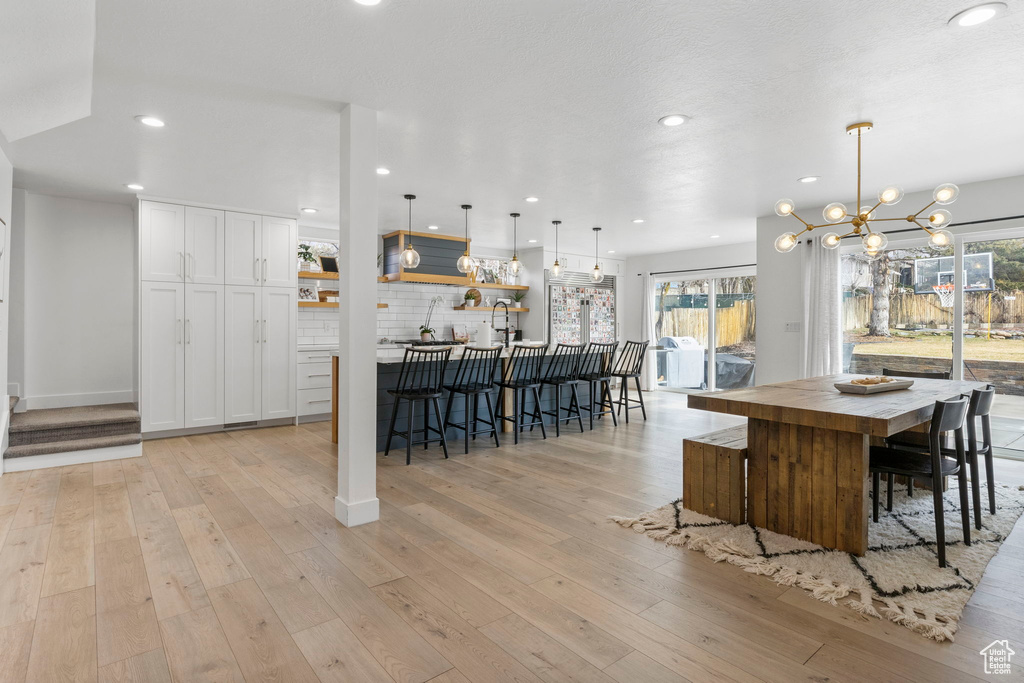 Kitchen with white cabinets, light hardwood / wood-style flooring, a notable chandelier, and a healthy amount of sunlight