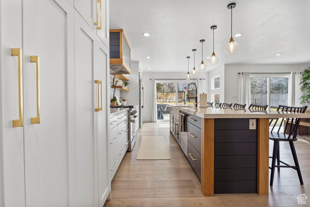 Kitchen with white cabinetry, hanging light fixtures, light hardwood / wood-style flooring, a kitchen island with sink, and a kitchen breakfast bar