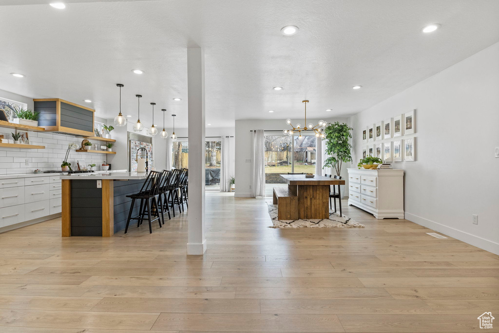 Interior space with light hardwood / wood-style flooring, a kitchen island with sink, white cabinetry, tasteful backsplash, and a breakfast bar