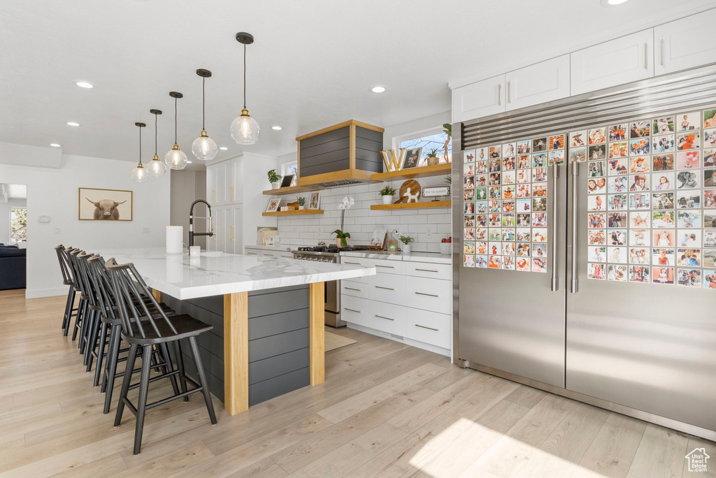 Kitchen with tasteful backsplash, light hardwood / wood-style floors, stainless steel appliances, and white cabinets