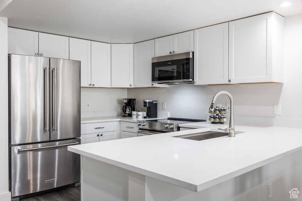 Kitchen featuring white cabinets, dark hardwood / wood-style flooring, sink, stainless steel appliances, and kitchen peninsula