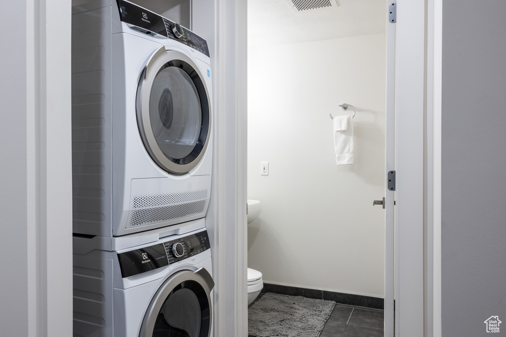 Laundry area featuring stacked washer and clothes dryer and dark tile flooring