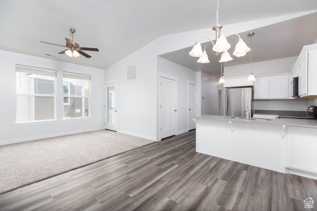 Kitchen with stainless steel refrigerator, white cabinets, stove, decorative light fixtures, and dark colored carpet