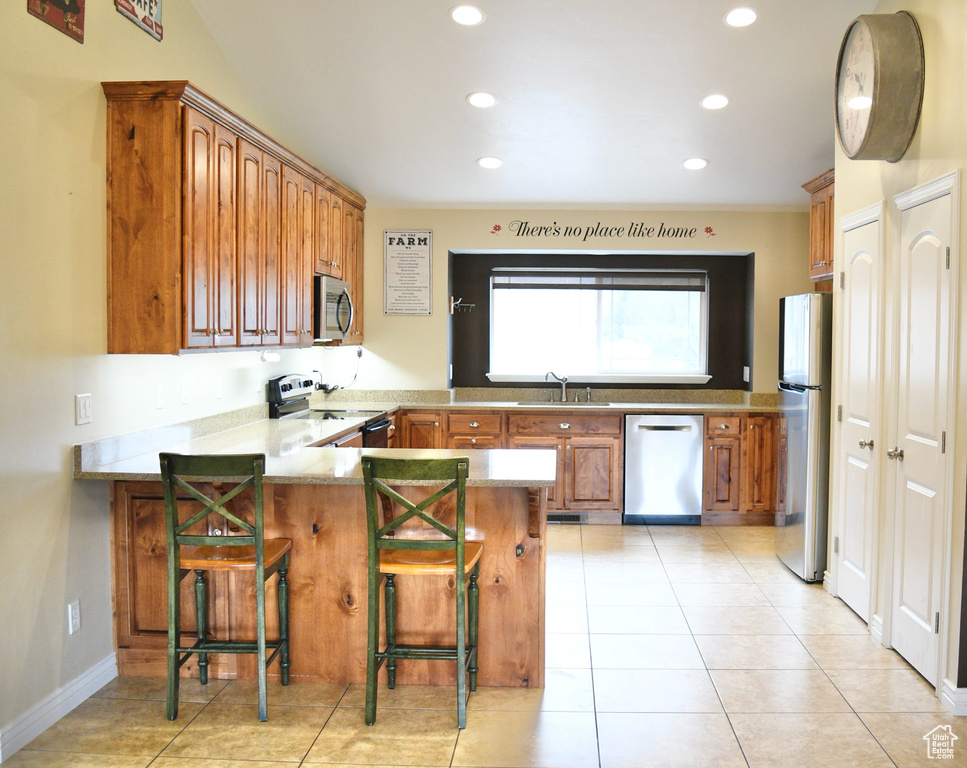 Kitchen featuring kitchen peninsula, appliances with stainless steel finishes, a breakfast bar, and light tile floors