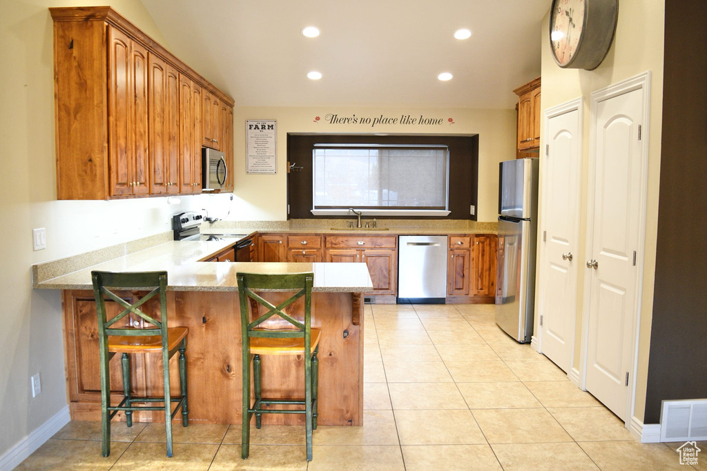 Kitchen with stainless steel appliances, a breakfast bar area, kitchen peninsula, sink, and light tile floors