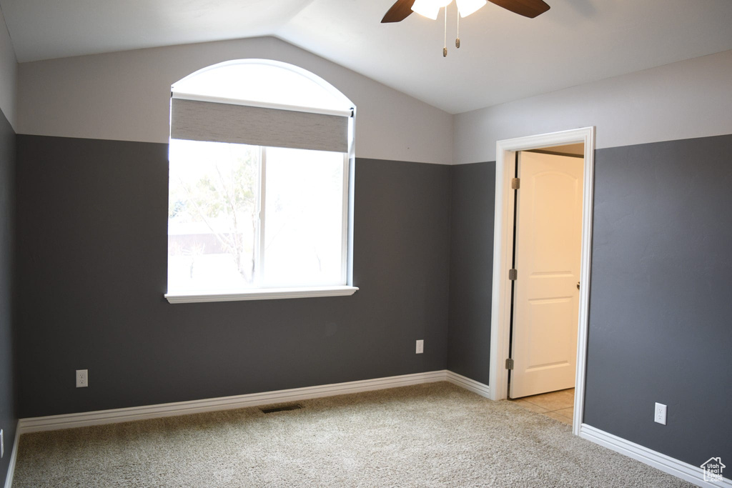 Spare room featuring plenty of natural light, lofted ceiling, ceiling fan, and light carpet