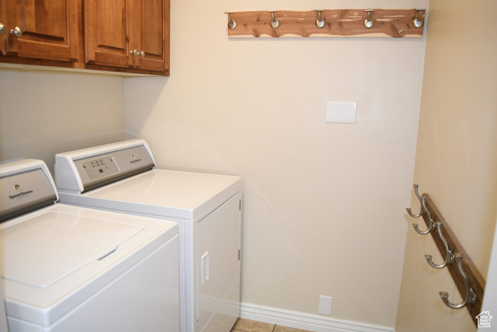 Clothes washing area with washer and clothes dryer, light tile floors, and cabinets