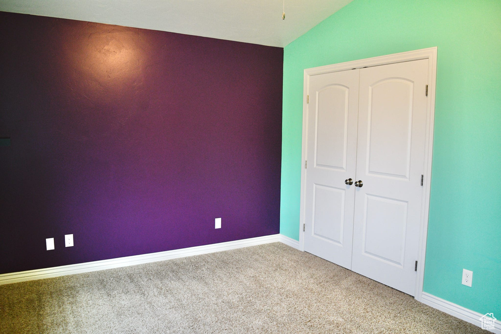 Unfurnished bedroom with vaulted ceiling, a closet, and light colored carpet