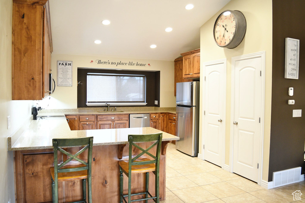 Kitchen with sink, a breakfast bar, stainless steel appliances, light tile floors, and kitchen peninsula