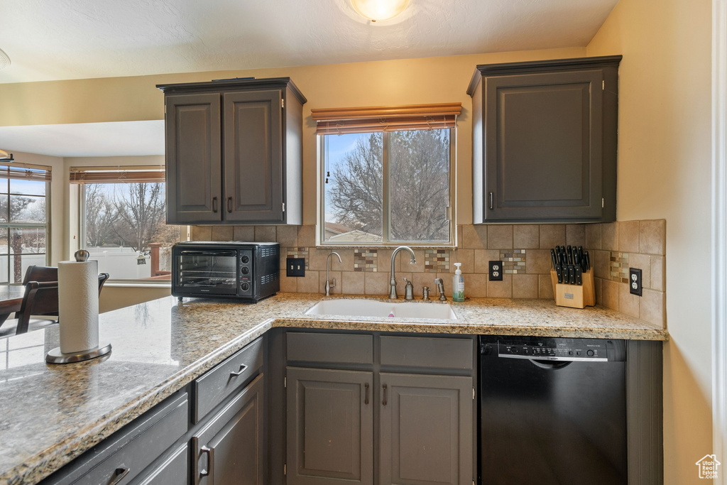 Kitchen featuring sink, light stone countertops, black dishwasher, and tasteful backsplash