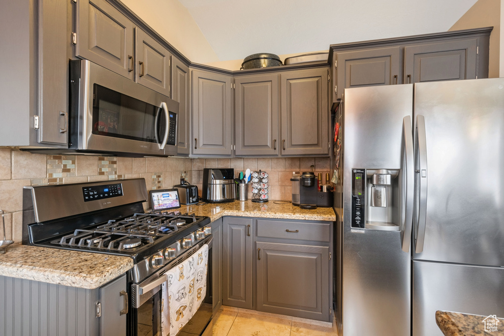 Kitchen with light stone countertops, light tile floors, stainless steel appliances, and backsplash