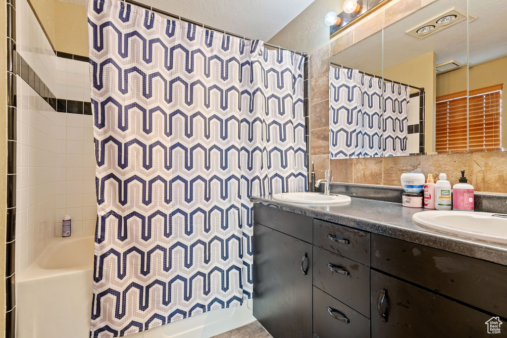 Bathroom featuring double vanity, tile walls, shower / tub combo, and tasteful backsplash