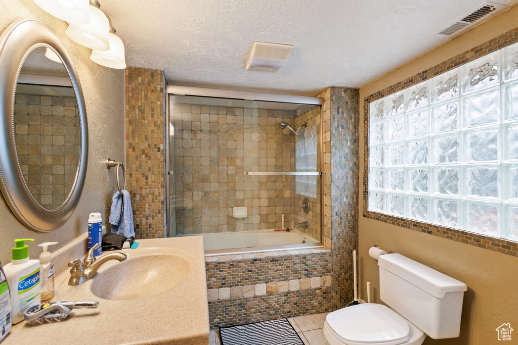Full bathroom with a textured ceiling, bath / shower combo with glass door, sink, toilet, and tile flooring