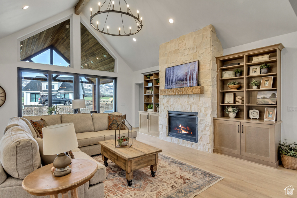 Living room featuring light wood-type flooring, an inviting chandelier, high vaulted ceiling, beam ceiling, and a stone fireplace