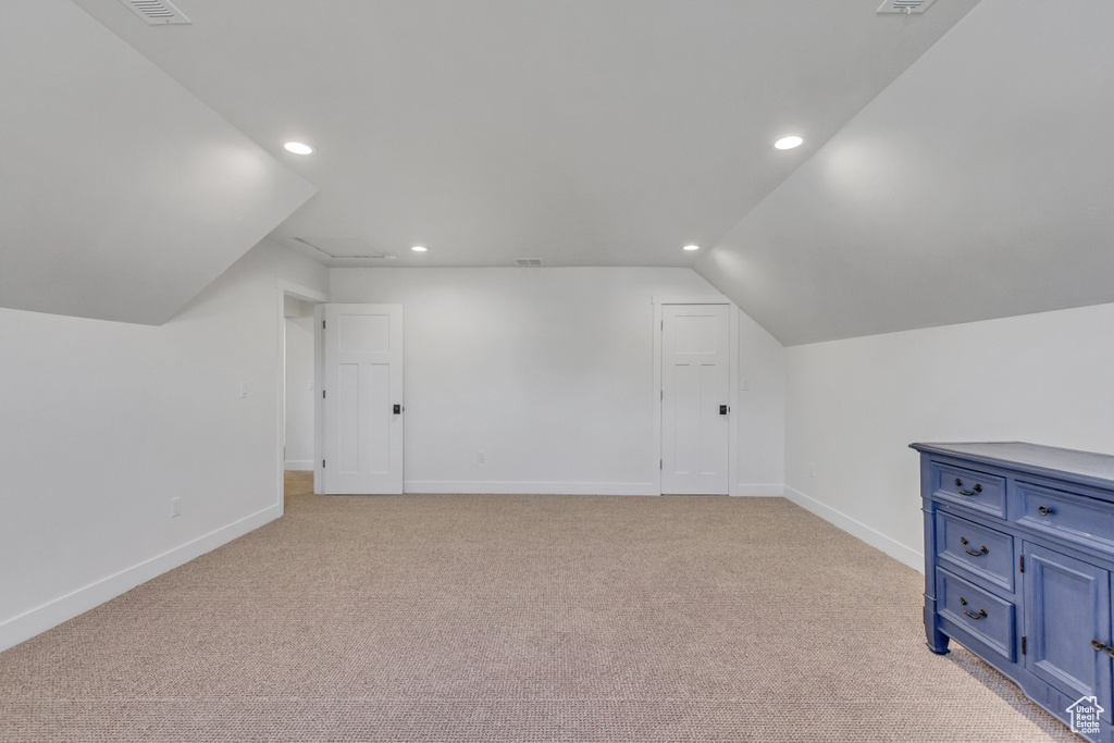 Additional living space with light carpet and vaulted ceiling