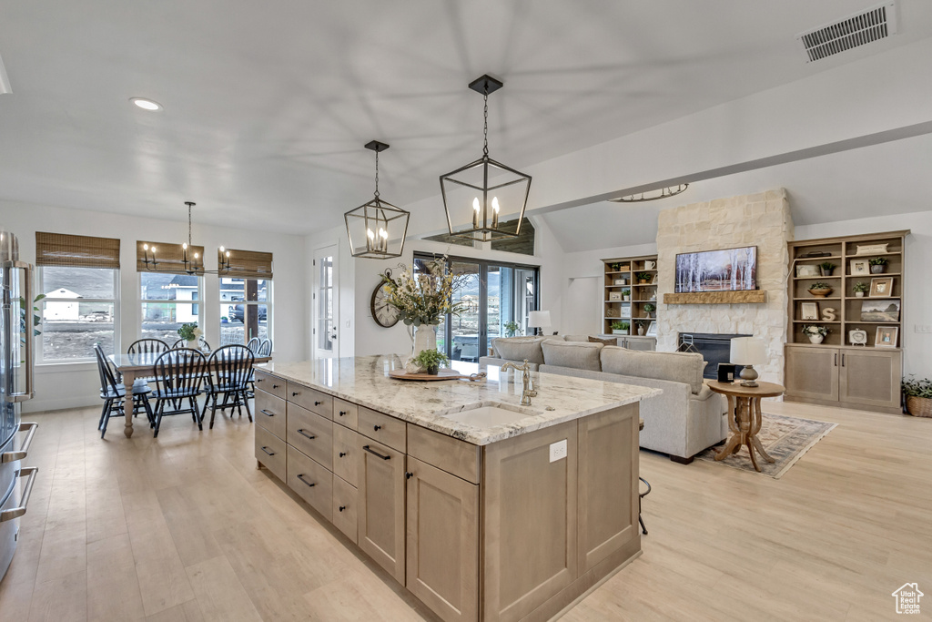 Kitchen featuring light wood-type flooring, an inviting chandelier, a center island, and a stone fireplace