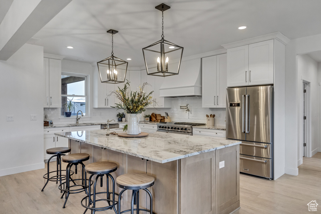 Kitchen with premium range hood, white cabinetry, light hardwood / wood-style flooring, high quality appliances, and a center island
