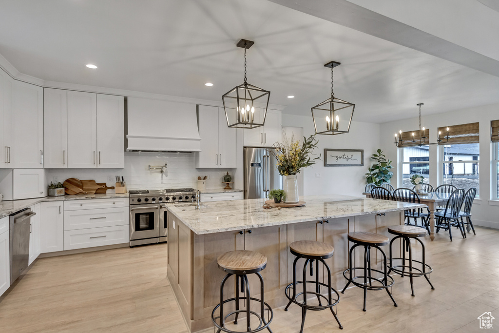 Kitchen featuring custom exhaust hood, white cabinets, a kitchen island, hanging light fixtures, and appliances with stainless steel finishes