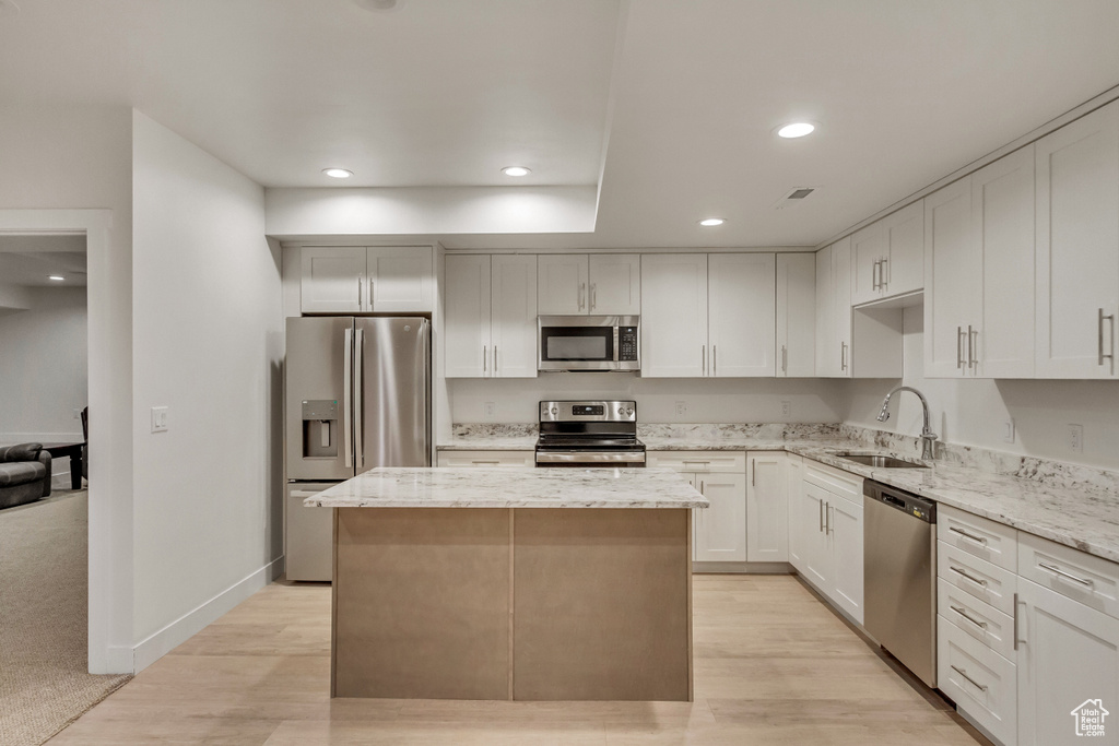 Kitchen featuring a center island, light stone countertops, stainless steel appliances, and light carpet
