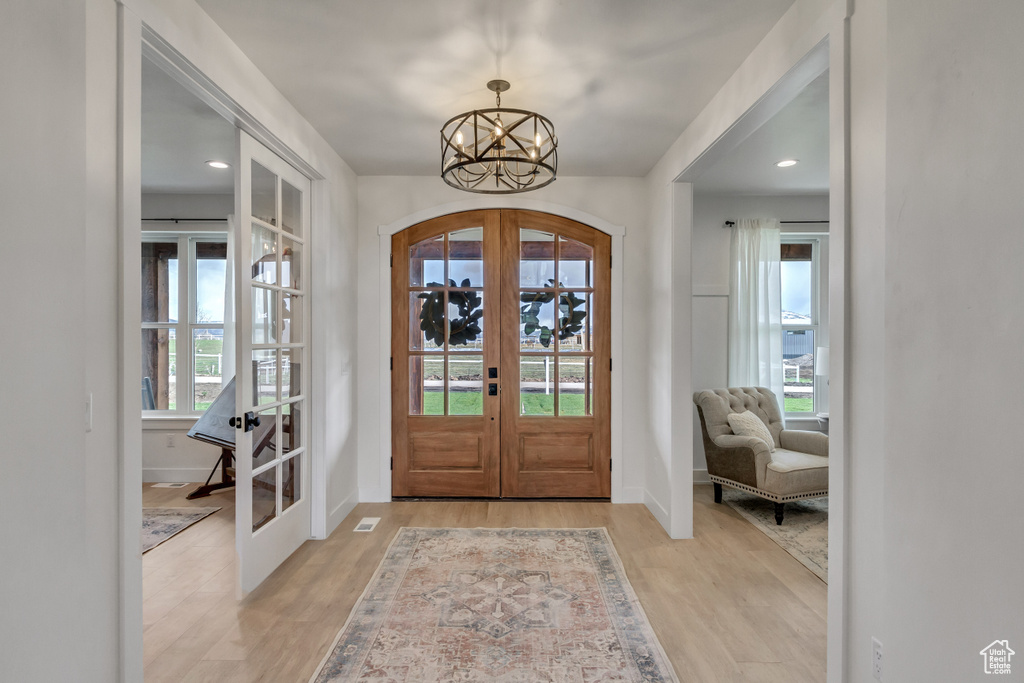 Foyer with an inviting chandelier, light hardwood / wood-style flooring, a wealth of natural light, and french doors