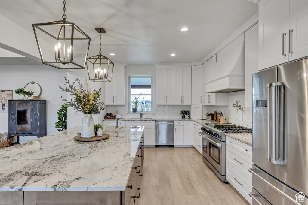 Kitchen featuring light stone counters, white cabinetry, light hardwood / wood-style flooring, premium appliances, and decorative light fixtures