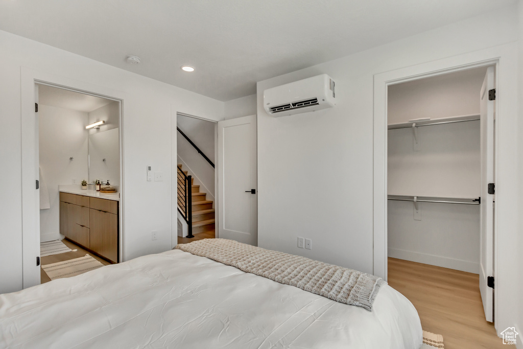 Bedroom featuring a spacious closet, light hardwood / wood-style flooring, a closet, a wall mounted AC, and ensuite bath