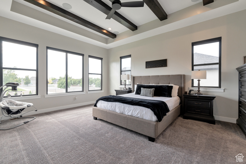 Carpeted bedroom with a tray ceiling, ceiling fan, beam ceiling, and multiple windows