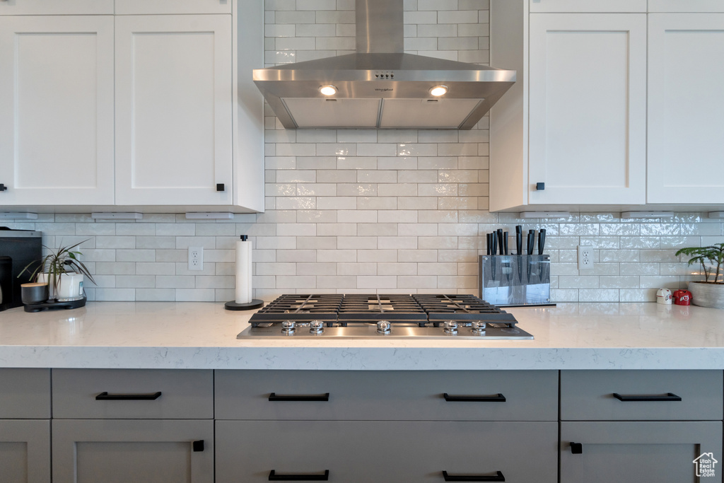 Kitchen featuring white cabinets, stainless steel gas stovetop, backsplash, and wall chimney range hood