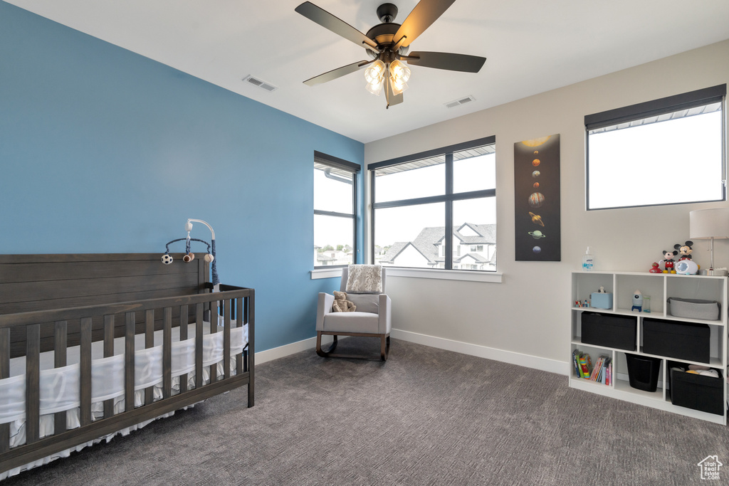Bedroom featuring dark colored carpet, ceiling fan, and a nursery area