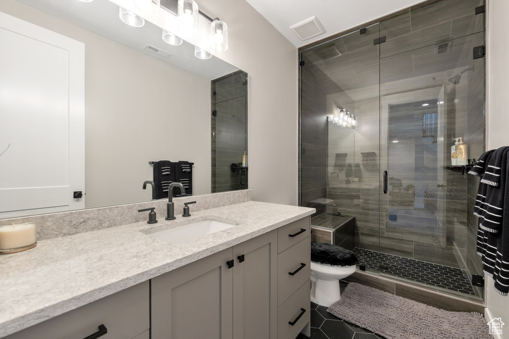 Bathroom featuring toilet, tile floors, an enclosed shower, and vanity with extensive cabinet space