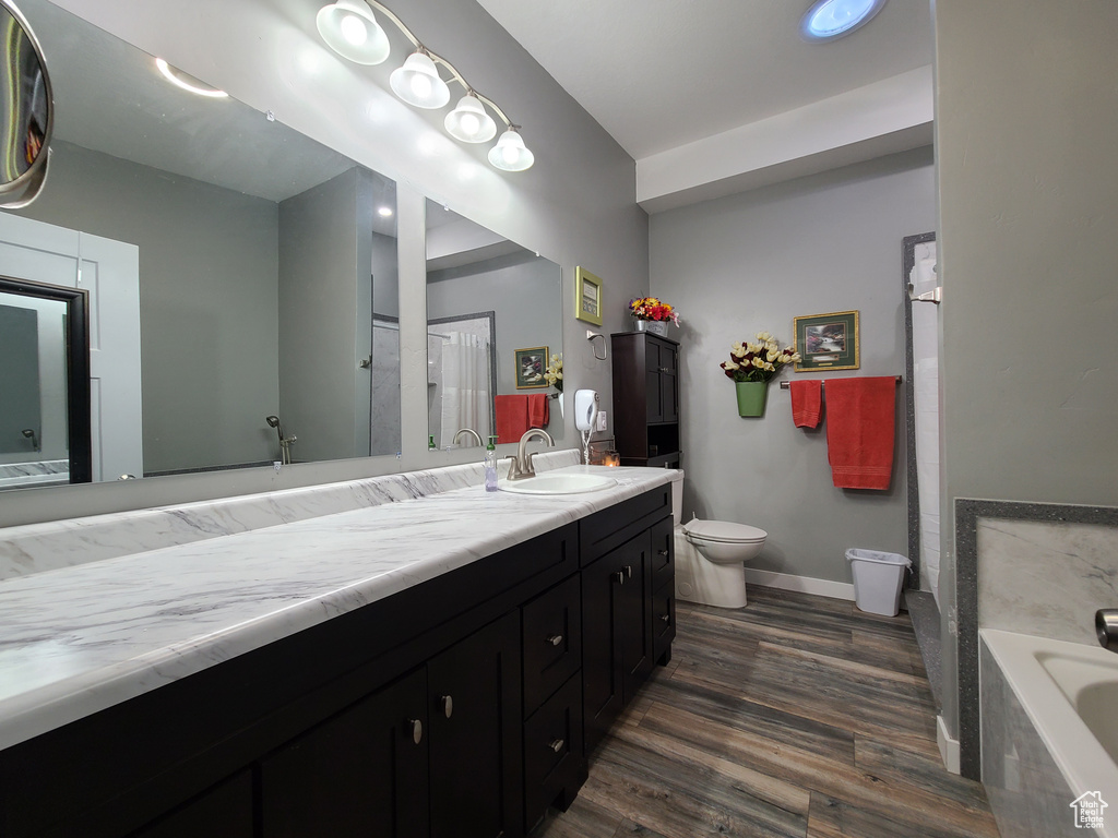 Bathroom featuring hardwood / wood-style floors, a washtub, vanity, and toilet