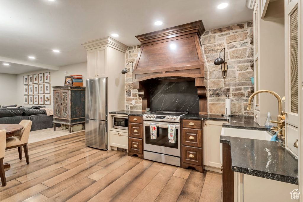 Kitchen with light hardwood / wood-style floors, custom range hood, sink, stainless steel appliances, and dark stone countertops