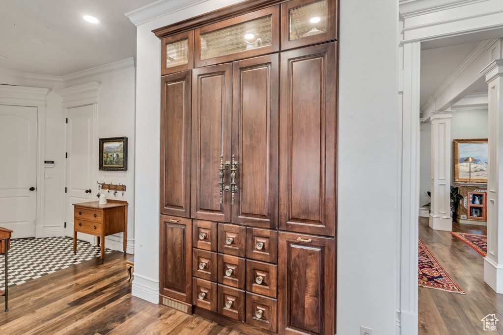 Interior space with crown molding, dark hardwood / wood-style floors, dark brown cabinets, and ornate columns