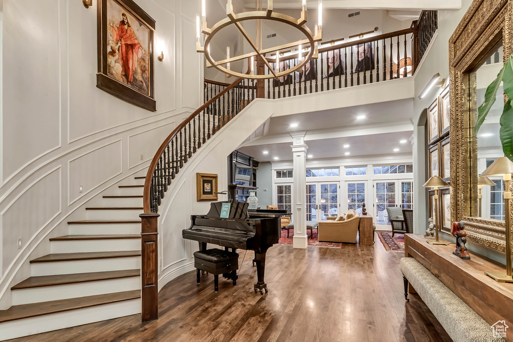 Foyer entrance featuring decorative columns, dark wood-type flooring, a notable chandelier, and a towering ceiling