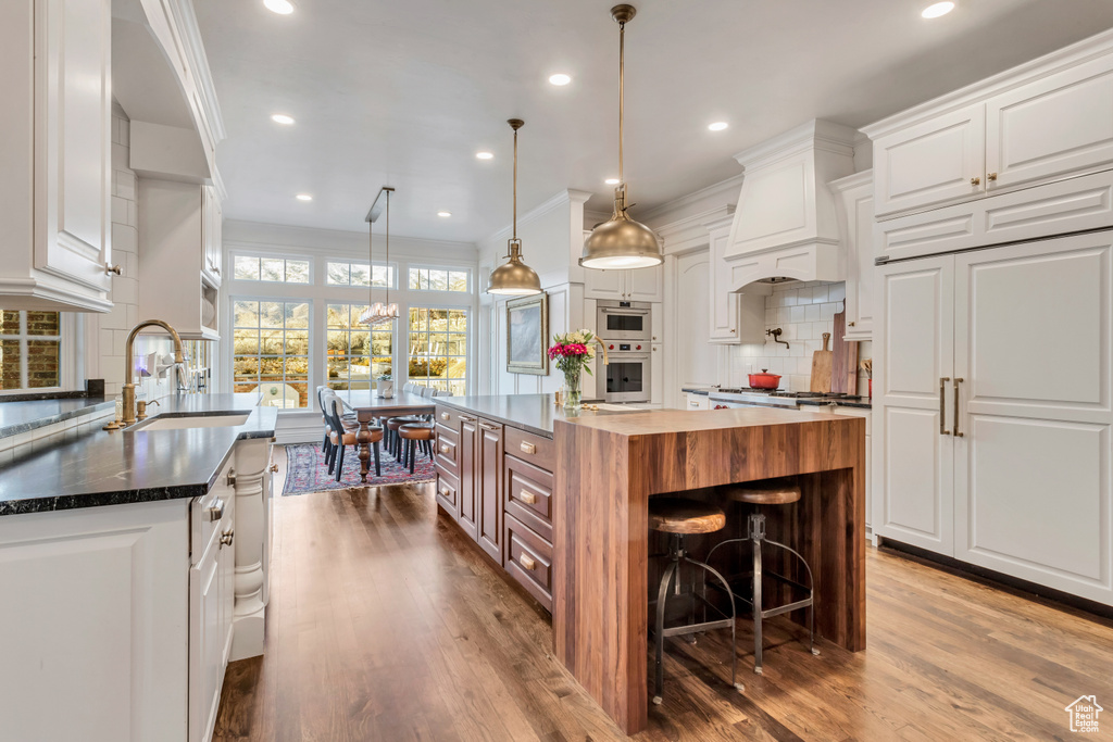 Kitchen with a kitchen island, crown molding, custom exhaust hood, white cabinetry, and wood-type flooring