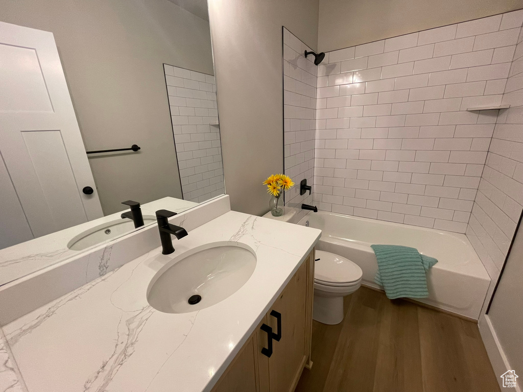 Full bathroom featuring tiled shower / bath, wood-type flooring, oversized vanity, and toilet