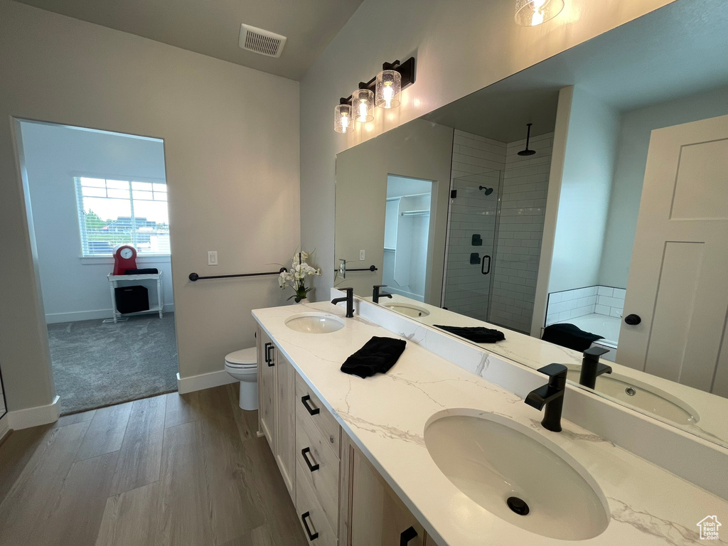 Bathroom featuring double sink vanity, wood-type flooring, an enclosed shower, and toilet