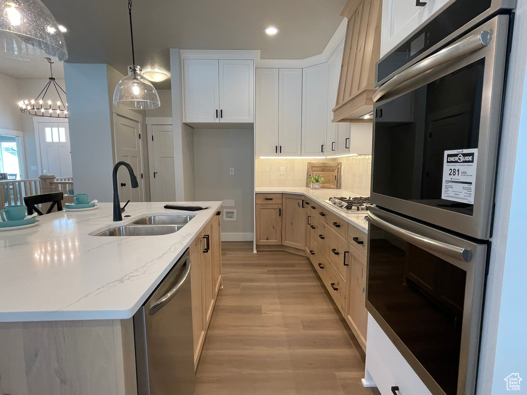 Kitchen featuring appliances with stainless steel finishes, light hardwood / wood-style flooring, a center island with sink, tasteful backsplash, and sink