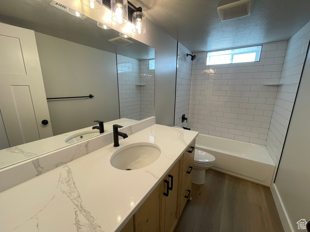 Full bathroom with tiled shower / bath, large vanity, a textured ceiling, toilet, and hardwood / wood-style flooring