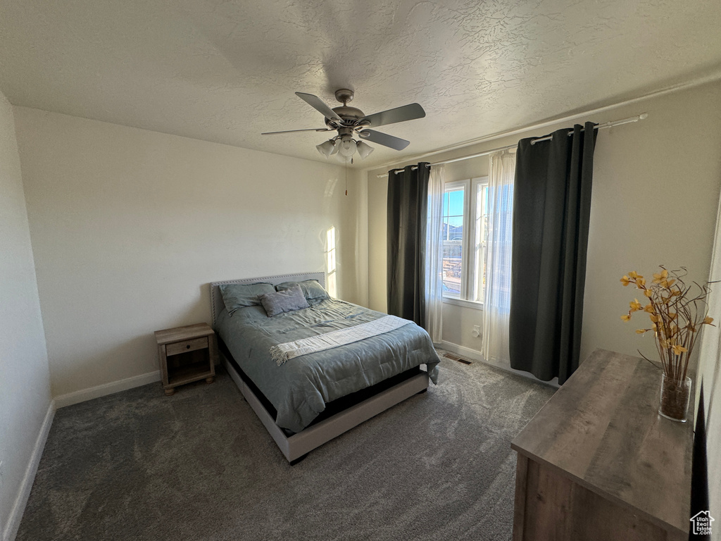 Bedroom with dark colored carpet, ceiling fan, and a textured ceiling