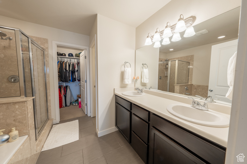 Bathroom featuring a shower with door, dual sinks, tile flooring, and vanity with extensive cabinet space